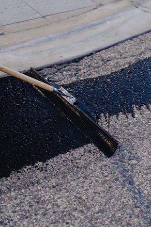 Close-up of a sealcoating squeegee applying sealant near a commercial cement sidewalk in an asphalt parking lot