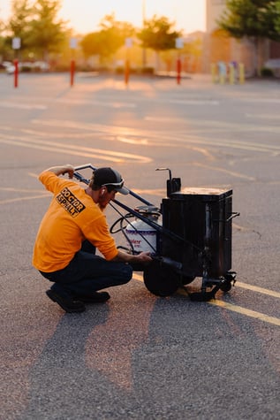 Doctor Asphalt paving professional using commercial-grade asphalt sealcoating maintenance equipment in a parking lot with visible line striping
