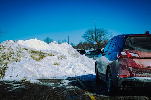 a large dirty snow pile from snow removal in a commercial parking lot with a car parked close nearby