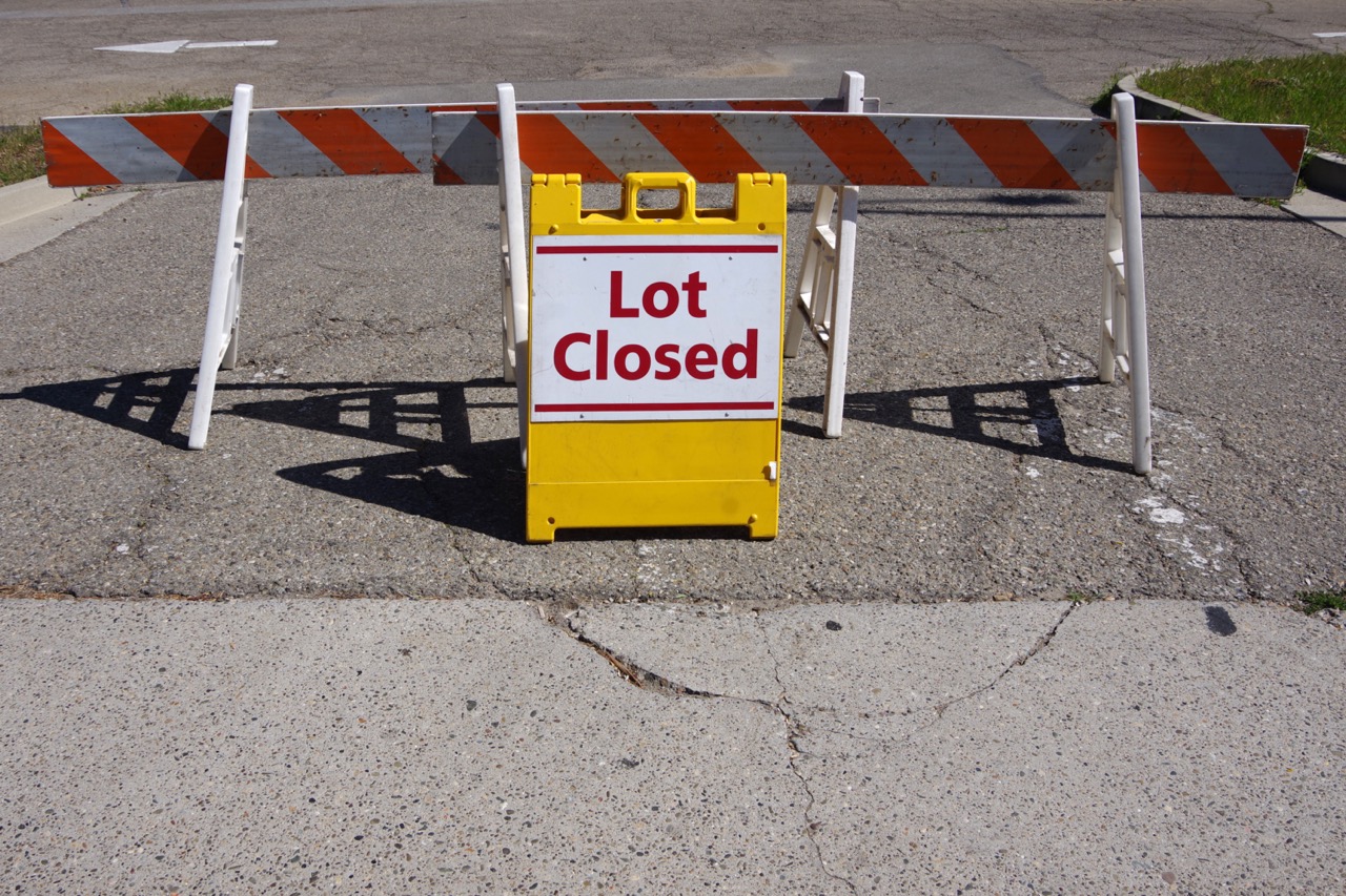 yellow lot closed sign and barricades in asphalt parking lot entrance
