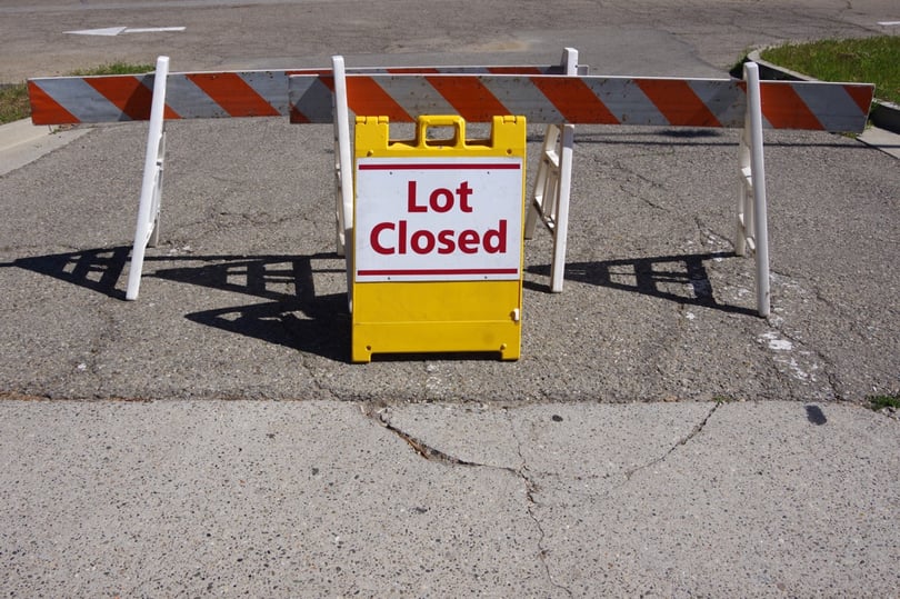 yellow lot closed sign and barricades in asphalt parking lot entrance
