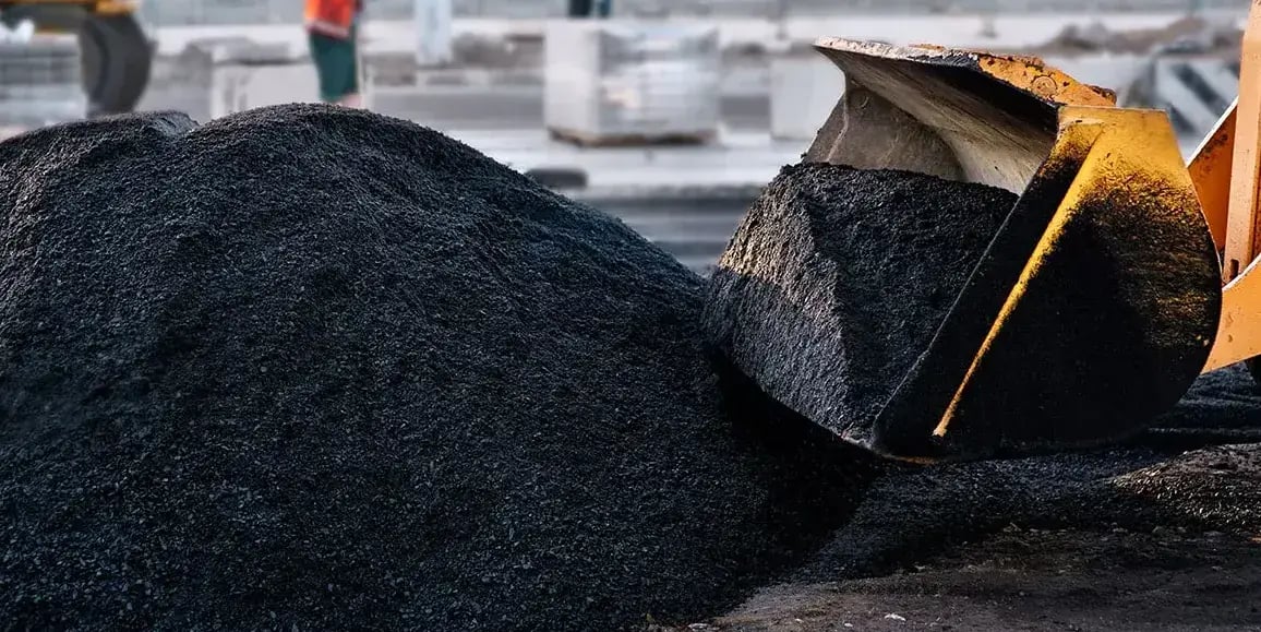 pile of black asphalt mix being moved by a yellow front loader in commercial parking lot