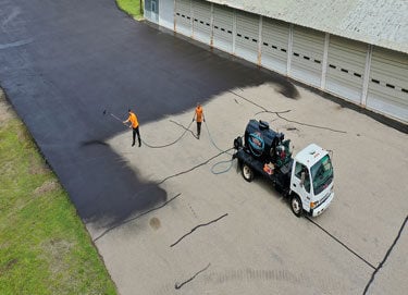 Seal coating being done in large apartment parking lot by Doctor Asphalt's crew