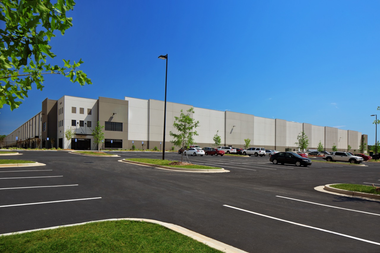 large parking lot in front of commercial warehouse distribution center building under blue sky