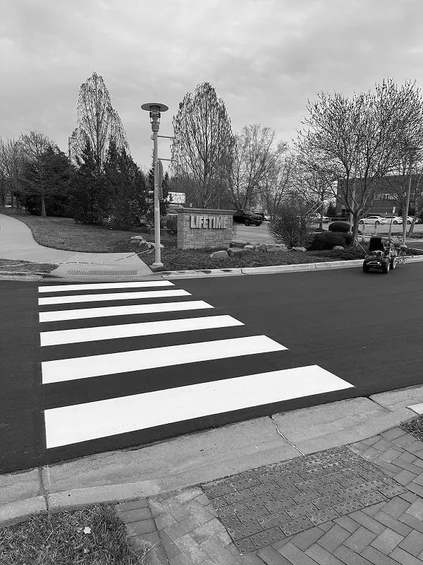 Freshly painted crosswalk striping on commercial roadway with striping machine in background
