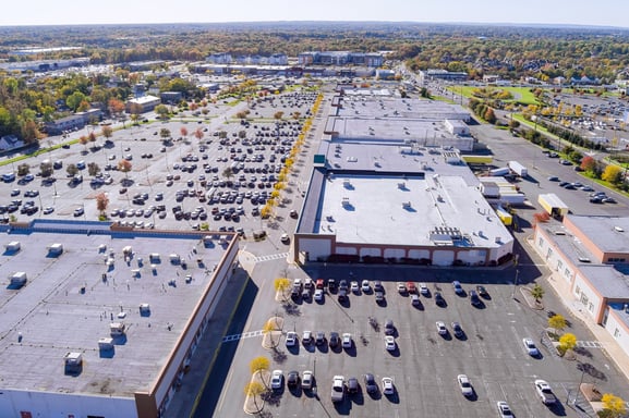 aerial view of a large retail shopping center with multiple buildings and parking lots with cars