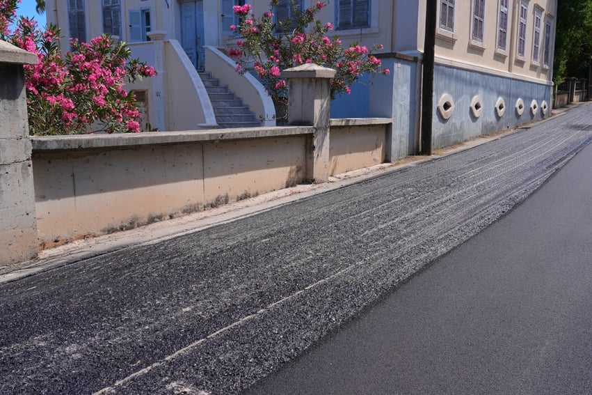 street with smooth overlay and rough milled asphalt pavement side by side during mill and overlay resurfacing process with building and pink flowers in the background