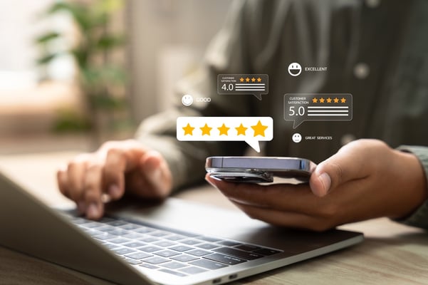 customer reviews and ratings graphics hovering above mobile device in a persons hand with a laptop nearby on desk