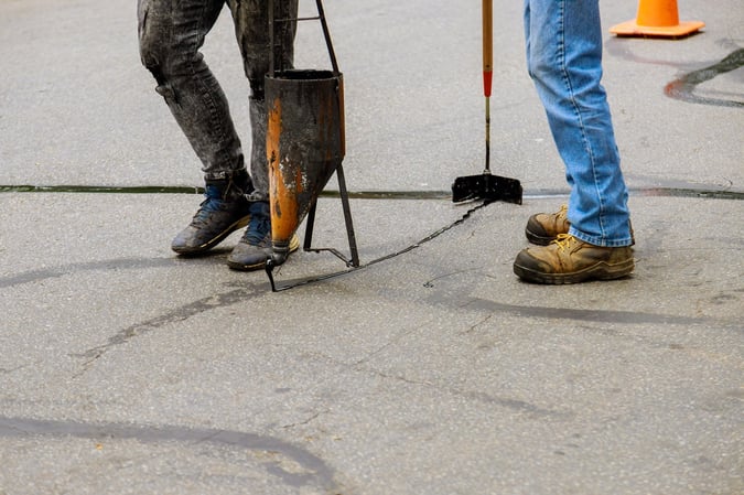 close up of the work boots of two commercial paving contractors crack filling asphalt pavement surface