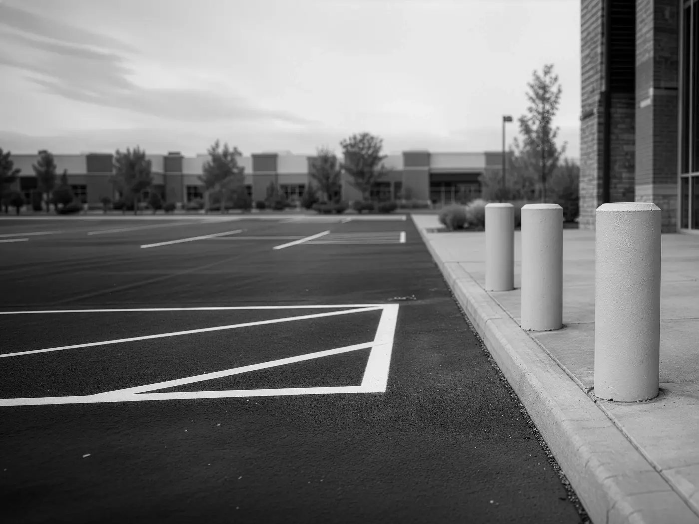 Concrete bollards installed along storefront curb next to freshly striped parking lot