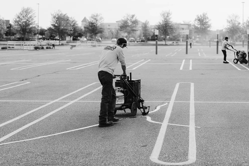 Doctor Asphalt crew member applying hot rubberized crack sealant with propane melter cart