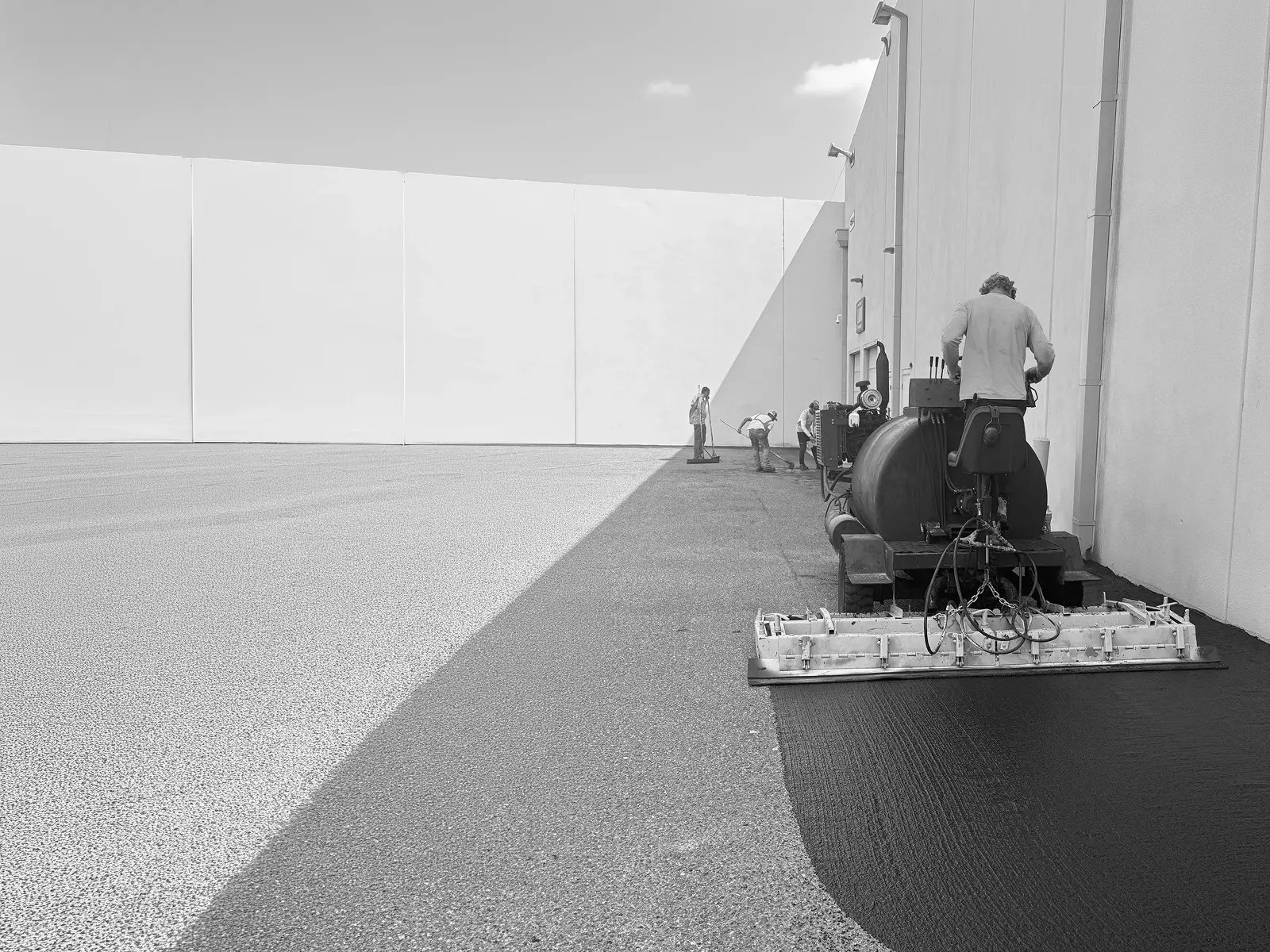 Doctor Asphalt crew applying microsurfacing with spreader box along building perimeter