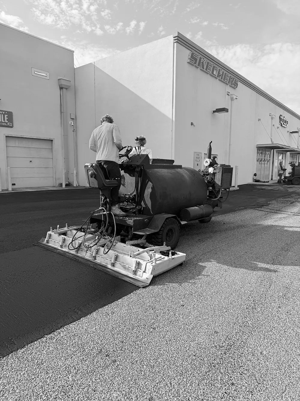 Doctor Asphalt crew operating microsurfacing spreader machine in retail center parking lot