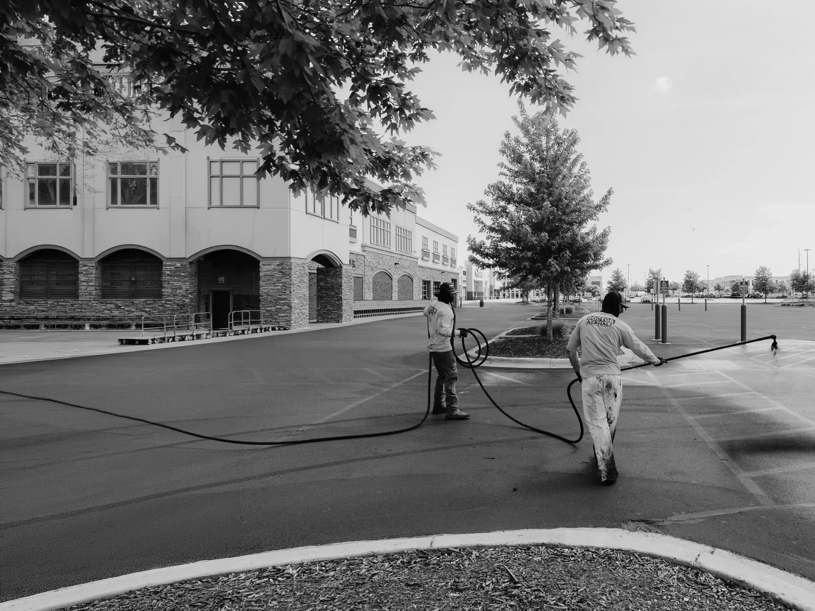 Doctor Asphalt crew sealcoating a commercial parking lot with spray hose equipment