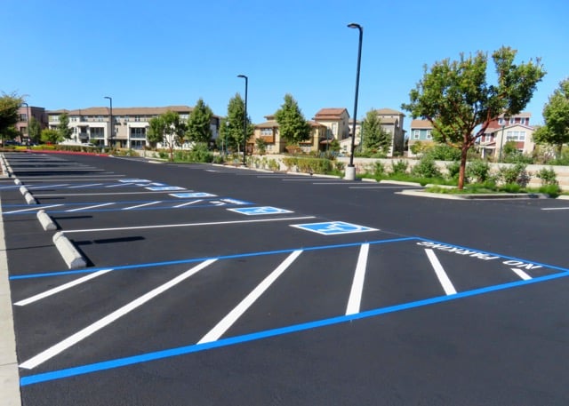 freshly paved commercial asphalt parking lot with white and blue line striping for ADA handicap parking spaces