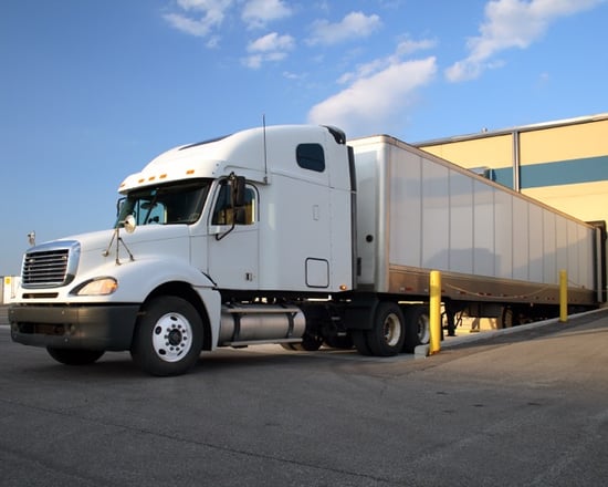 large white semi truck backed in to commercial loading dock at industrial warehouse
