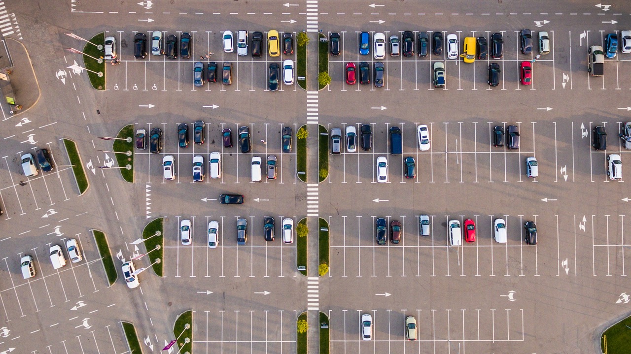 aerial view of large commercial parking lot with parked cars, pedestrian walk ways and entrance driveways