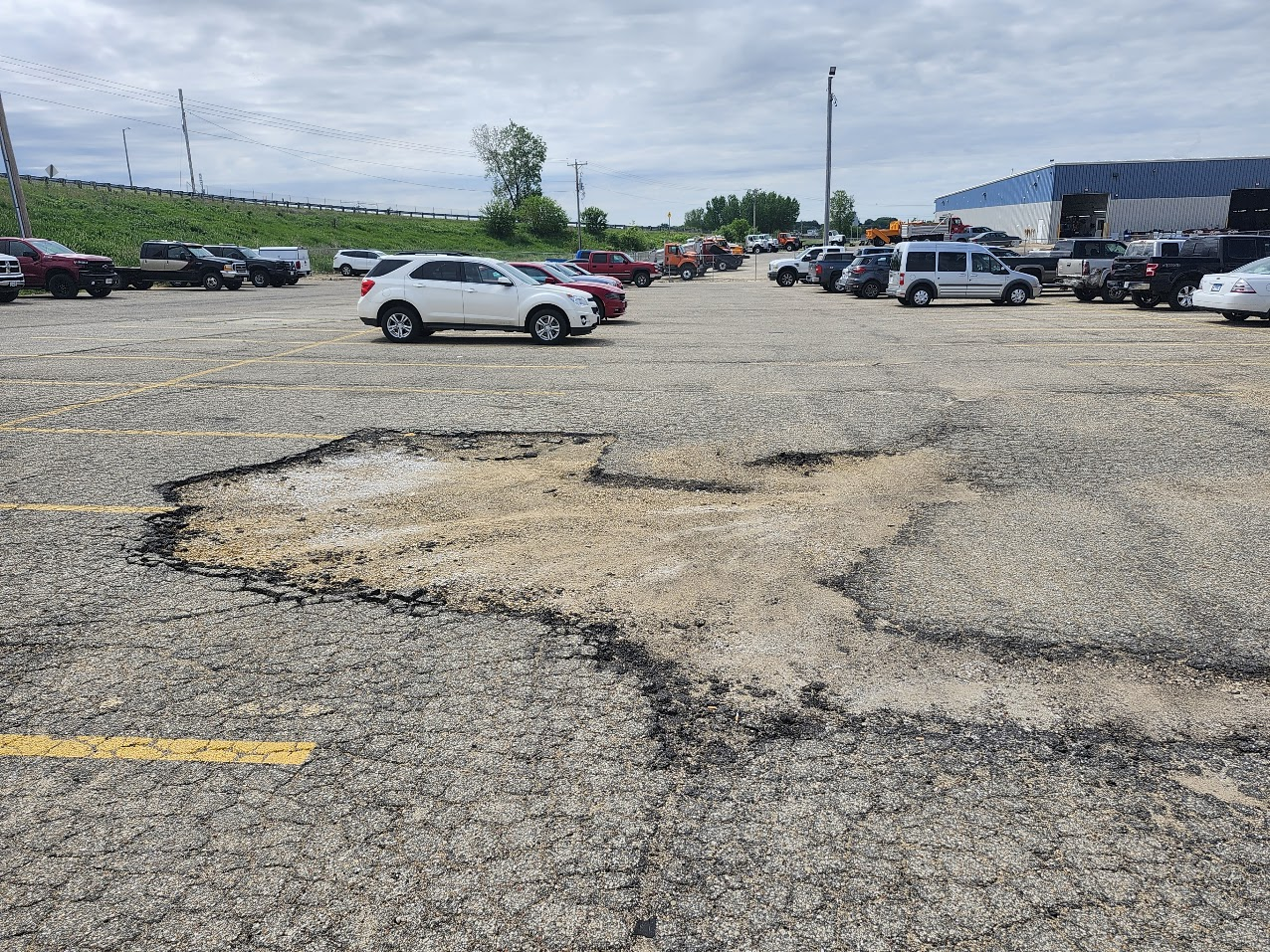 Severe asphalt deterioration and a massive pothole in a commercial parking lot.