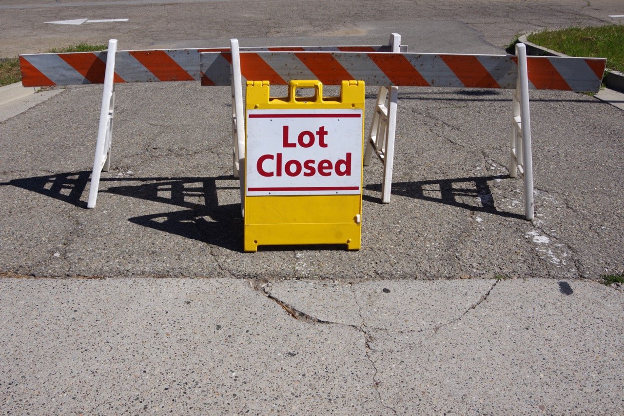 yellow lot closed sign and barricades in asphalt parking lot entrance